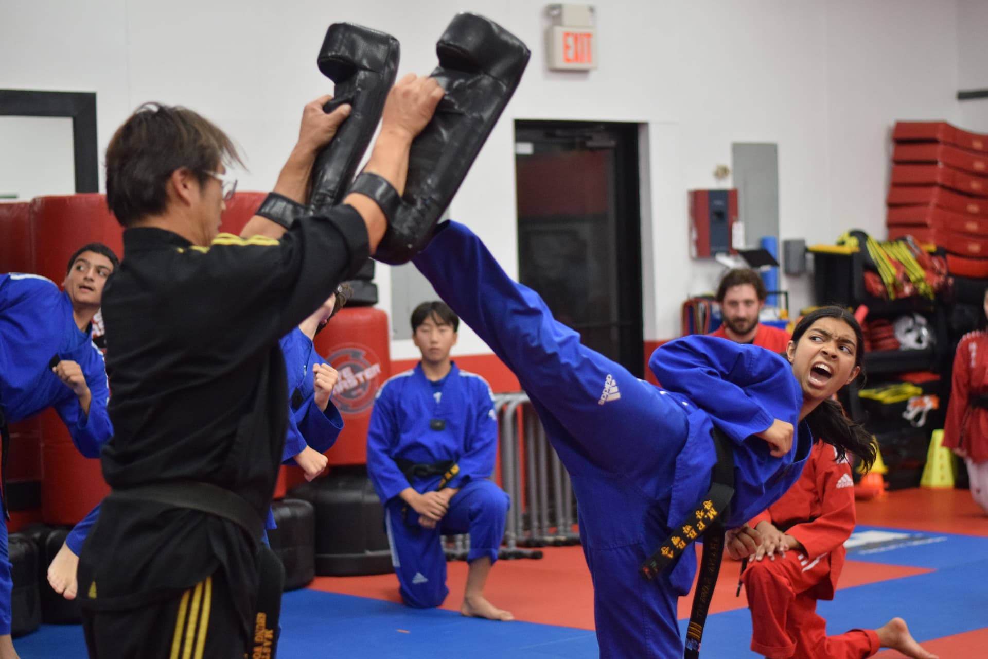 Instructor holding striking pads while a student throws a kick during class
